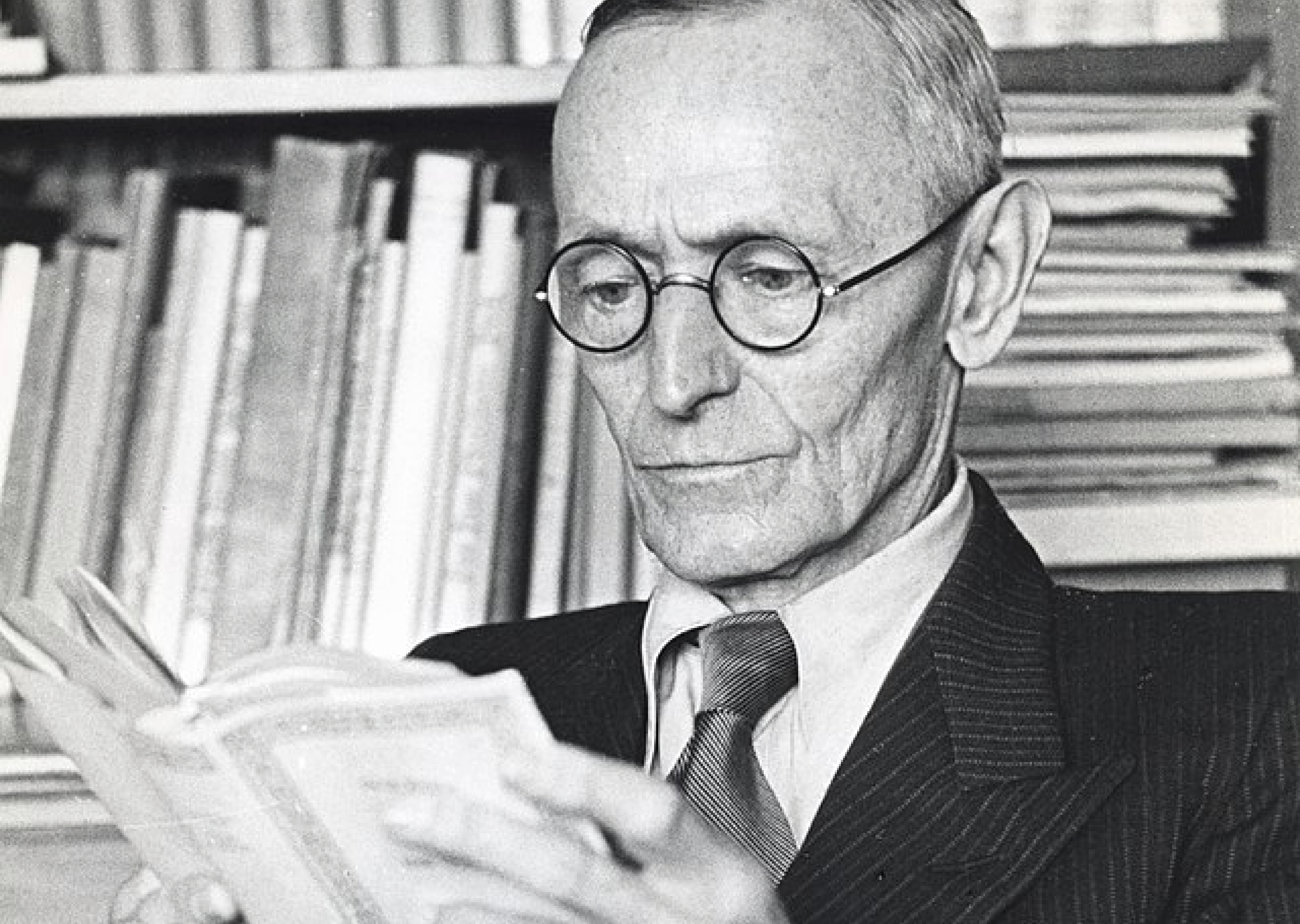 Auf dem Schwarz-Weiß-Foto ist Hermann Hesse mit Brille zu sehen, der ein Buch in den Händen hält und liest.