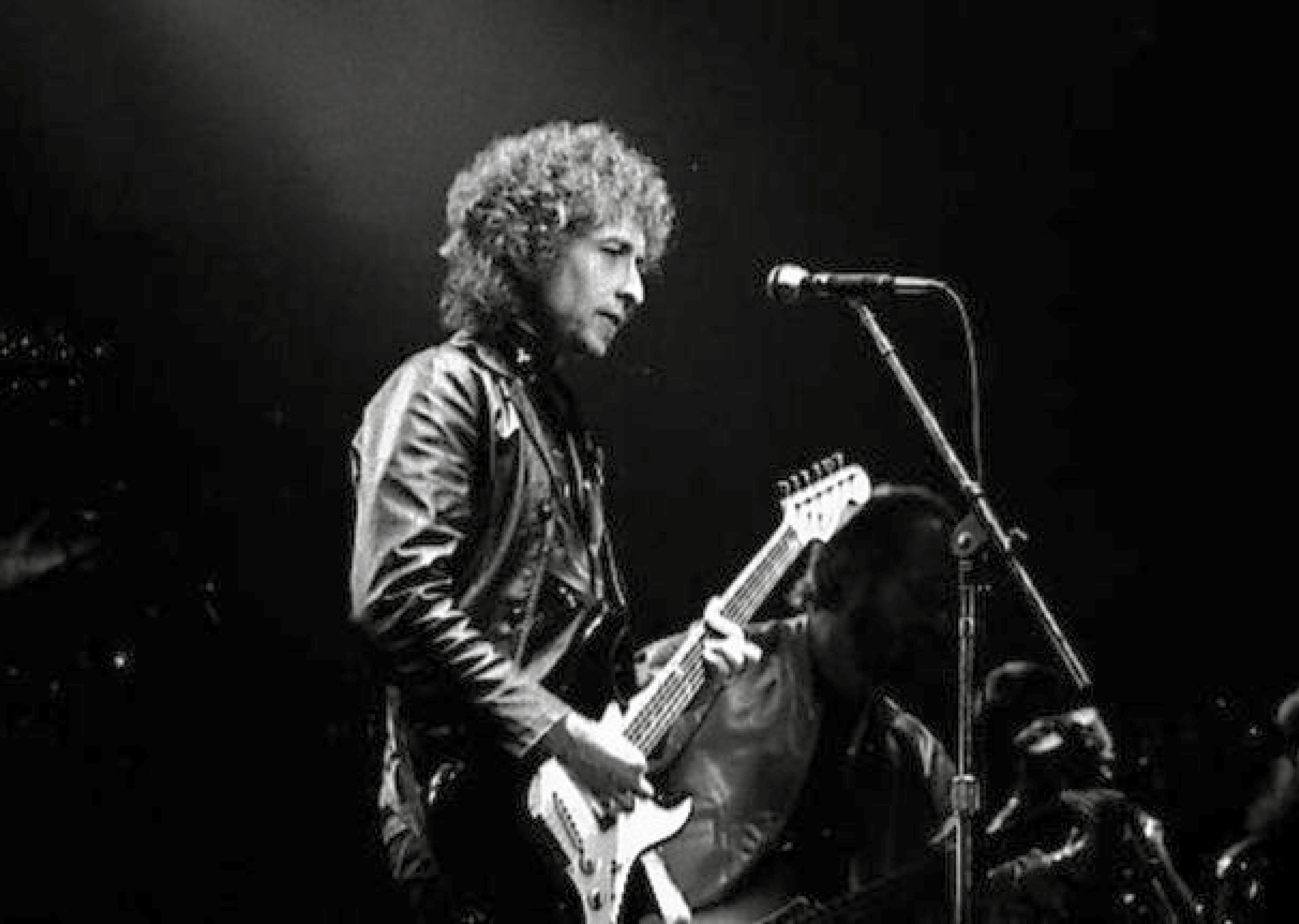 Auf dem Schwarz-Weiß-Foto steht Bob Dylan mit einer E-Gitarre auf der Bühne.